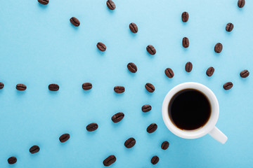 Cup of Coffee with rays of coffee beans on blue background. Flat lay. Morning black coffee mood...