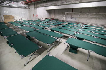 Camp folding cots are being set up in the underground parking of a stadium