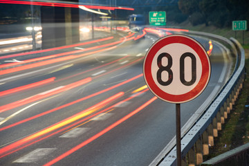 Long exposure shot of traffic sign showing 80 km/h speed limit on a highway full of cars in motion blur during the night - obrazy, fototapety, plakaty