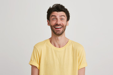 Obraz premium Close up of happy and very excited attractive young brunet with beard eyebrows raised wears yellow casual tshirt, isolated over white background