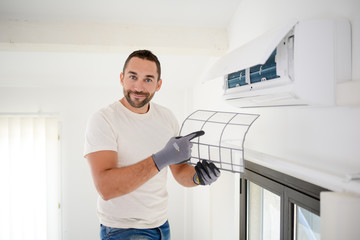handsome young man electrician cleaning air filter on an indoor unit of air conditioning in a...