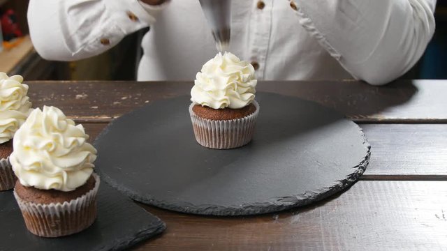 Baker decorating tasty cupcake with cream at table. Food and confectionery concept