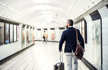 Rear view of businessman with a bag and suitcase walking in subway.