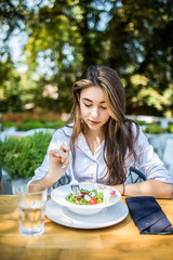 Smiling woman eating fresh salad in restaurant outdoors