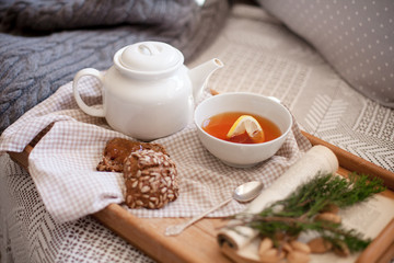 Fototapeta na wymiar Autumn or Christmas still life in cozy home interior. Morning breakfast with white teapot, bowl of lemon tea, rye bread with seeds. Healthy food are serving on wooden tray on sofa with knitted sweater