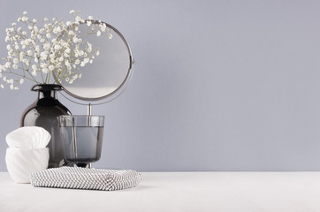 Modern elegant female dressing table with black glass vase with flowers, mirror, silver cosmetic bag on grey color wall and white wood board.