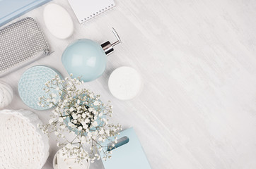 Elegant cosmetics set of accessories for beauty care - soap, towel, soap dispenser, pastel blue bowls, silver cosmetic bag, white flowers on white wood background, top view.