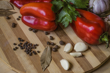 Red bell pepper, celery, bay leaf with garlic and scented pepper  lie on a striped wooden cutting board

