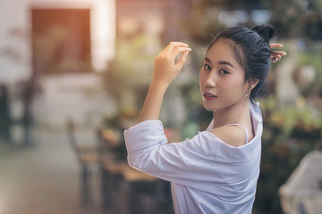 Asian pretty girl. She was wearing a white shirt. Is post posture and look sweet and charming. In an atmosphere of lush trees and the evening sun outside of the coffee shop with copy space.