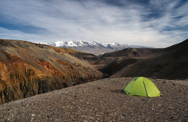 Camp tent in dramatic dark desert steppe on a highland mountain plateau on a horizon snow peaks