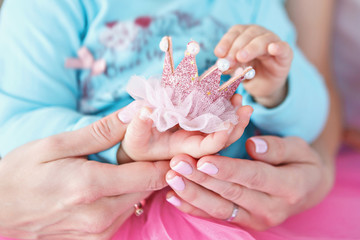 Baby girl and her mother holding little pink crown. Soft focus