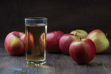 Glass of apple juice with red apples on wooden table, closeup