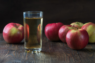 Glass of apple juice with red apples on wooden table, closeup