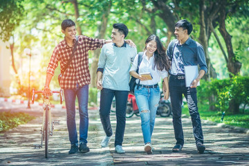 Fototapeta premium A group of Asian student was walking on the road within the University. They talk to smile happily and motivate the bicycle to walk together. In the shade of trees streets and the sun in the afternoon