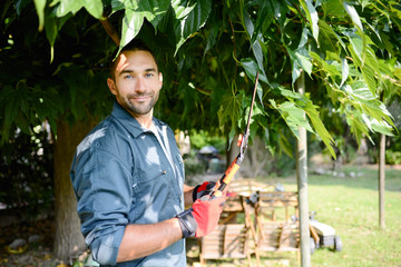 handsome young man gardener trimming hedgerow in a garden park outdoor