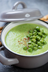 Close-up of cream-soup with green peas served in a pot, vertical shot, selective focus