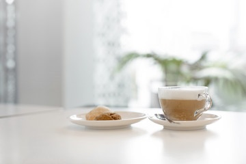 Transparent cup with cappuccino near the plate with cookies on plant background cafe