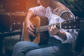 Asian girls wearing white shirts and jeans. She is sitting on a black couch is currently vacationing by playing guitar in a coffee shop.