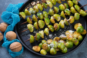 Skewers with roasted brussels sprouts, grated parmesan and walnuts on a metal tray, studio shot