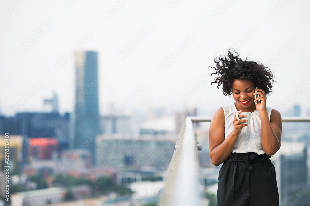 Poster A portrait of a woman with coffee and smartphone standing on a terrace.