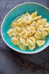 Turquoise bowl with tortellini in bouillon, vertical shot over grey asphalt background