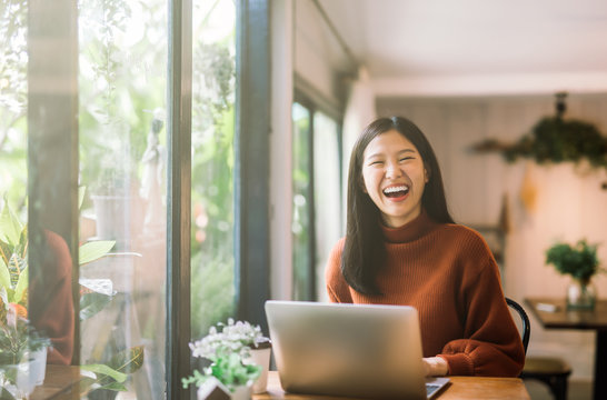 Happy Young Asian Girl Working At A Coffee Shop With A Laptop