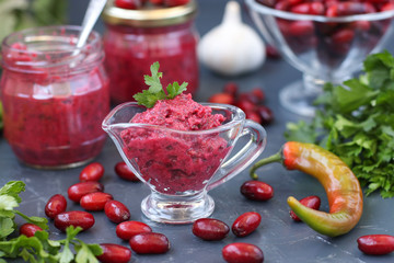 Dogwood sauce in sauceboat. On the table is also dogwood in a vase, sauce in cans, garlic, parsley and chili pepper. Tkemali sauce