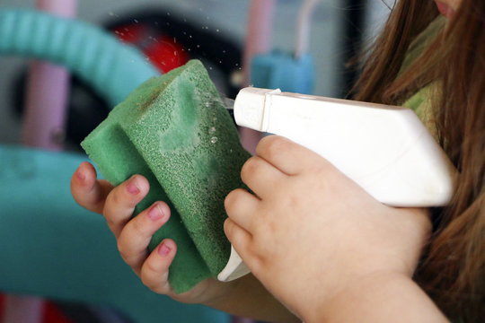 the baby is doing wet cleaning. sprinkles washing liquid onto a sponge from a plastic bottle.