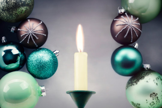  Weihnachtskugeln in braun und in Grüntönen stapeln sich hinter einer Kerze