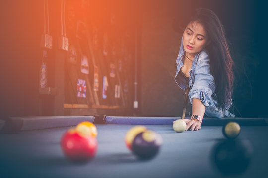 Asian girl with long hair wearing a jacket and jeans. Are aiming to play pool on the pool table, which is made of blue flannel with copy space