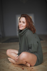 Indoor portrait of young smiling beautiful woman enjoying time at scandinavian style home, sitting on the on the floor in warm green sweater. Golden Christmas confetti on hair.