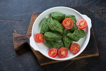 Plate of fried vegetable nuggets with spinach on a rustic wooden serving board, horizontal shot on a dark brown stone surface