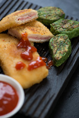 Close-up of sliced chicken cordon bleu with fried vegetable nuggets, vertical shot, selective focus