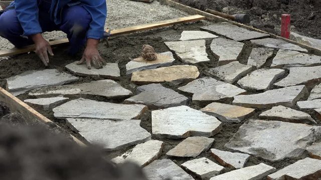 Mason worker making sidewalk pavement with stone blocks