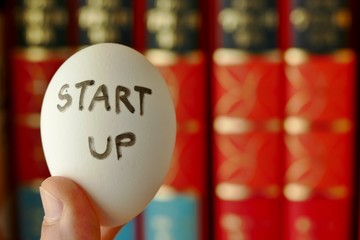 nurturing or incubator startup concept. startup word wrote on the egg shell with the background of text book