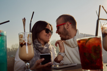 Couple using cellphone while drinking coffee outdoors.