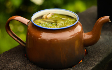 Tea mashed in a vintage tea pot on an old cooker, close up view with focus on currant leaves added to impart delicate aroma and flavor.