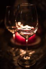 Close-up of two empty wine glasses standing against the backdrop of burning candles on a festive table during Happy New Year celebration.