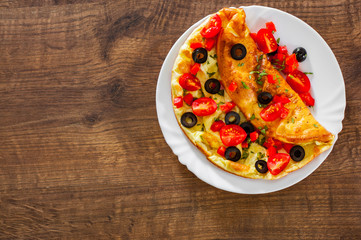 omelette with tomato, pepper and olive in white plate on wooden table background