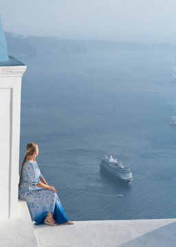Happy woman in white and blue dress enjoying her holidays on Santorini, Greece. View on Caldera and Aegean sea from Imerovigli.