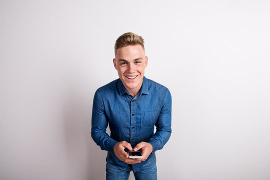 Portrait of a happy young man in a studio, holding smartphone.