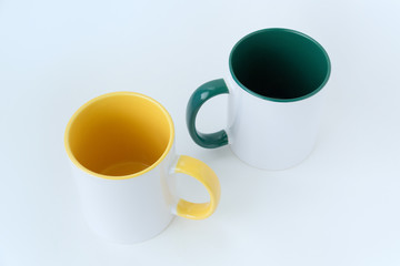 Two white mugs, with a green and yellow handle on a white background.  Isolated.  View from above.