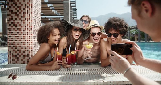 Guy filming a video of his friends in swimming pool drinking cocktails and chatting. always online 4k