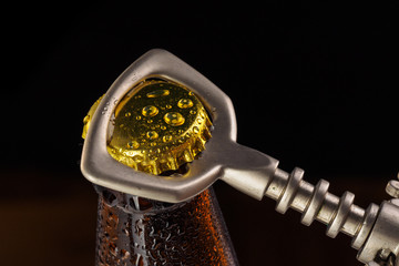 A hand opening a fresh cold ale bottle of beer with drops and stopper open with bottle opener on...