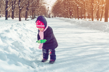 Fototapeta na wymiar Little girl with a snow shovel playing outside in winter