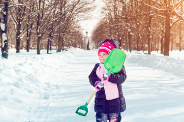 Fototapeta na wymiar Little girl with a snow shovel playing outside in winter
