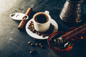 Cup of coffee, coffee beans, ashtray with cigar on dark background