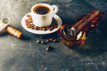 Cup of coffee, coffee beans, ashtray with cigar on dark background