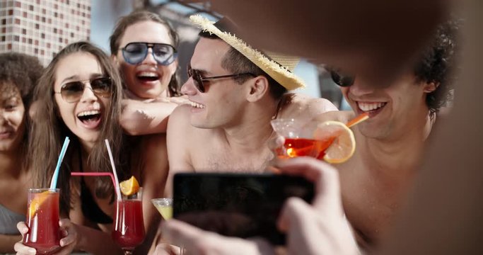 Guy filming a video of his friends in swimming pool drinking cocktails and chatting. always online 4k