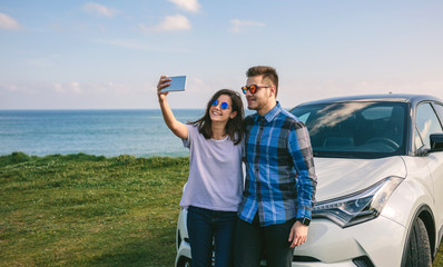 Young couple doing a selfie leaning on the car near the coast